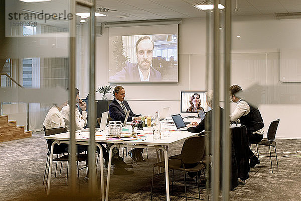 Führungskräfte aus der Wirtschaft diskutieren in einer Sitzung während einer Webkonferenz durch Glas im Büro gesehen