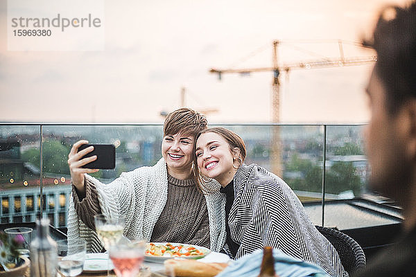 Lächelnde Freundinnen  die sich beim geselligen Beisammensein auf der Terrasse mit einer Decke durchs Telefon führen