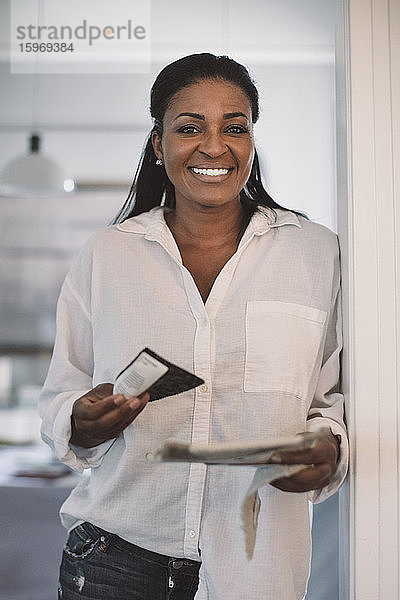Porträt einer lächelnden Geschäftsfrau mit Stoffmuster im Heimbüro stehend