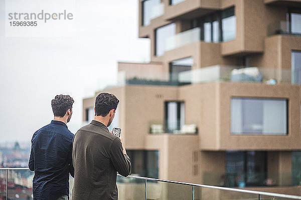 Mann fotografiert mit einem Smartphone  während er bei einem Freund auf der Terrasse steht