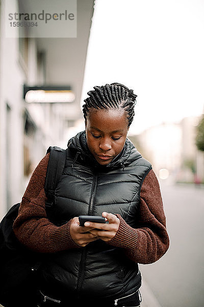 Teenager-Mädchen benutzt Smartphone beim Spazierengehen auf einem Fußweg in der Stadt