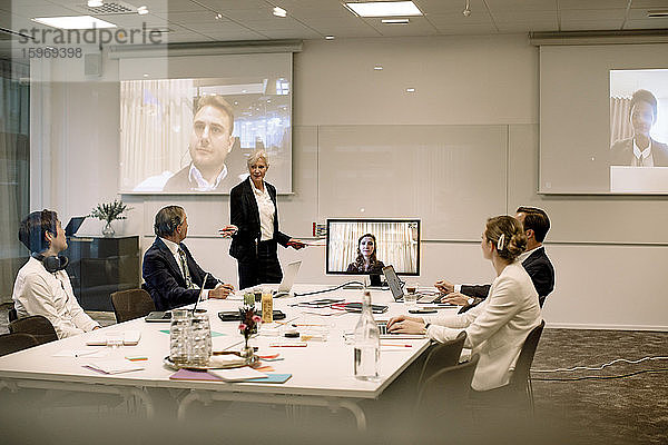 Reife Geschäftsfrau hält Präsentation vor Kollegen im Sitzungssaal während einer globalen Konferenzsitzung im Büro