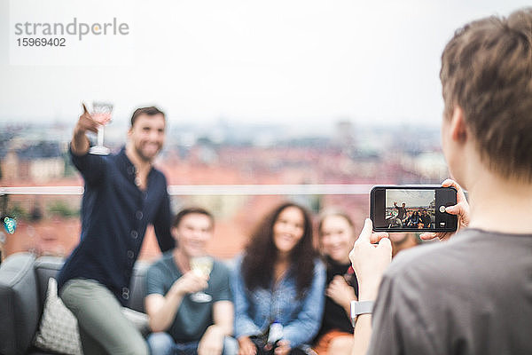 Rückansicht einer Frau  die während einer Terrassenparty Freunde per Handy fotografiert