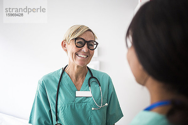 Lächelnder reifer Kinderarzt im Gespräch mit weiblicher Mitarbeiterin im Stehen in der Klinik