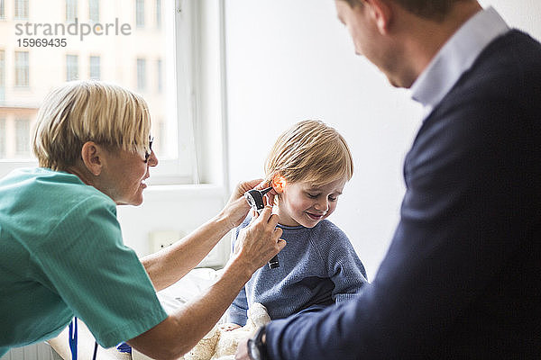 Ärztin untersucht das Ohr des Jungen mit dem Otoskop  während sie im Krankenhaus beim Vater sitzt
