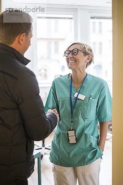 Lächelnde Ärztin schüttelt reifer Patientin die Hand  während sie in der Klinik steht