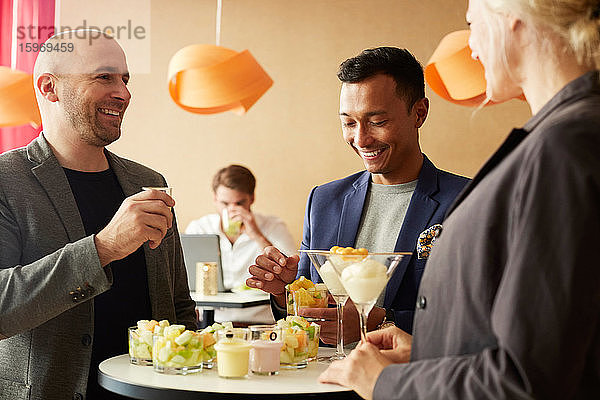 Lächelnde Geschäftsleute unterhalten sich beim Essen im Büroseminar