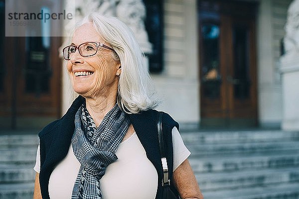 Lächelnde ältere Frau schaut weg  während sie die Stadt erkundet