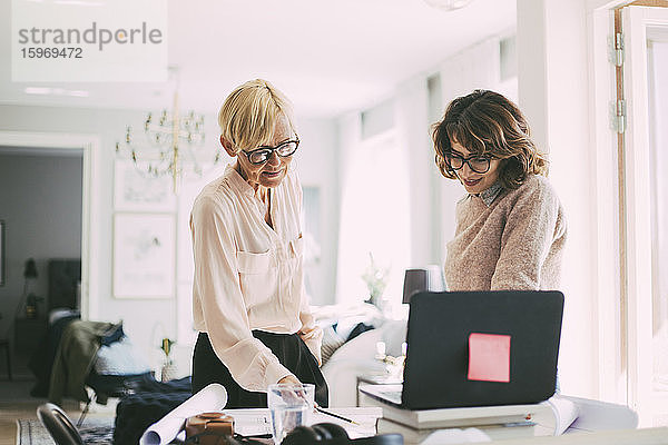 Zwei Frauen stehen am Arbeitsplatz im Wohnzimmer und arbeiten zu Hause