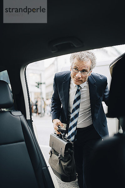 Reifer männlicher Unternehmer steigt während einer Geschäftsreise in ein Taxi