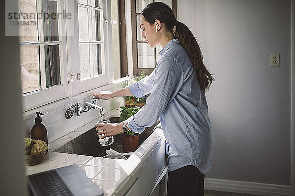 Seitenansicht einer weiblichen Geschäftsfrau  die Wasser in einen Krug an der Küchenspüle füllt