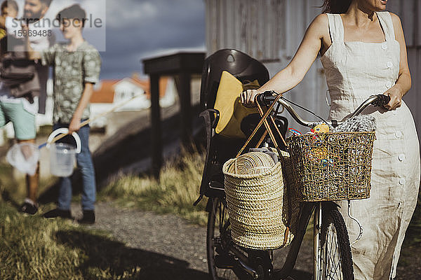 Mitschnitt einer Frau mit Fahrrad  während die Familie im Hintergrund auf dem Archipel steht