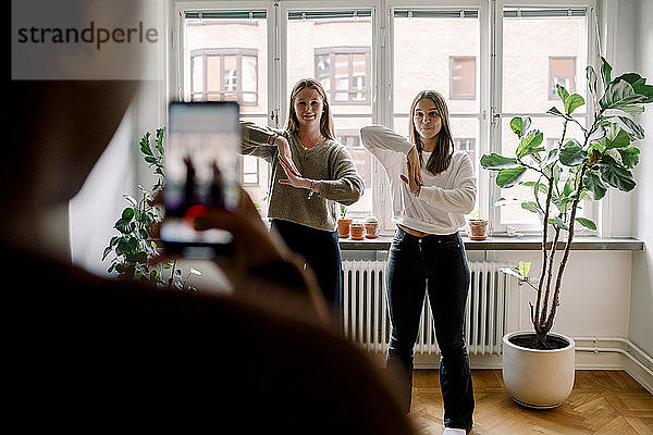 Teenager-Mädchen mit Handy filmt Freundinnen  die im Wohnzimmer gegeneinander tanzen