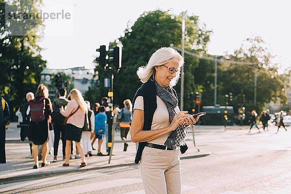 Lächelnde  faltige Frau mit Smartphone auf der Straße in der Stadt