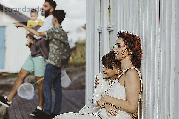 Lächelnde Mutter umarmt Sohn  während die Familie im Hintergrund steht