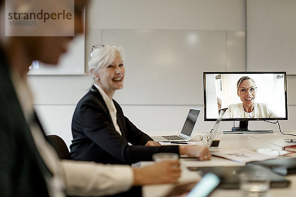 Lächelnder weiblicher Manager diskutiert mit Kollegen per Webkonferenz während eines globalen Geschäftstreffens