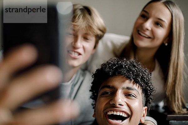 Fröhliche männliche und weibliche Freunde im Teenageralter  die sich mit dem Handy zu Hause selbstständig machen