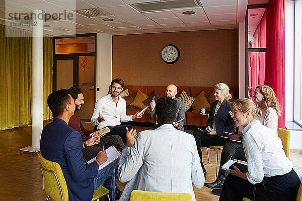 Lächelnde Unternehmer diskutieren im Kreis sitzend im Büro-Workshop