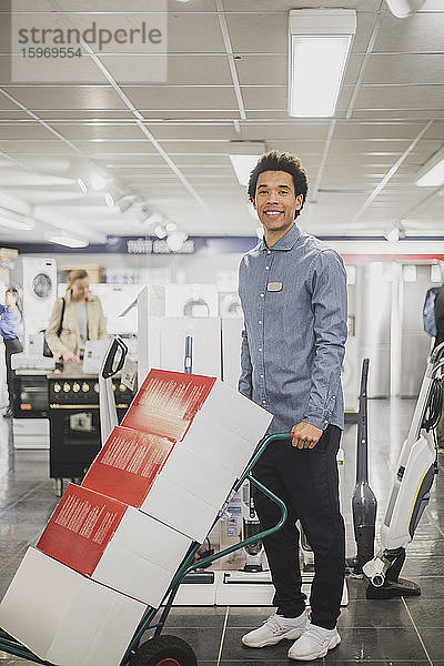 Porträt eines lächelnden männlichen Besitzers mit Gepäckwagen im Elektronikladen