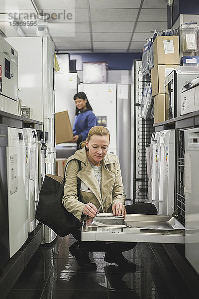 Reife Kundin schaut auf Ofen  während sie im Elektronikladen hockt