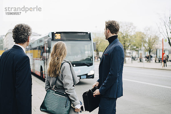 Unternehmerinnen mit männlichen Mitarbeitern  die in der Stadt stehend auf den Bus schauen