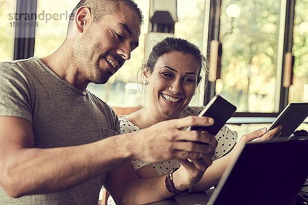 Lächelnder Mann zeigt der Partnerin im Café ein Smartphone