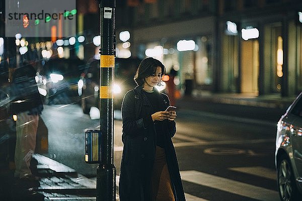 Frau surft am Telefon im Netz  während sie nachts in der Stadt steht