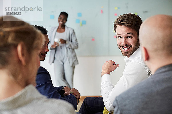 Lächelnder Geschäftsmann schaut männlichen Kollegen während einer Präsentation an  während er im Büroseminar sitzt