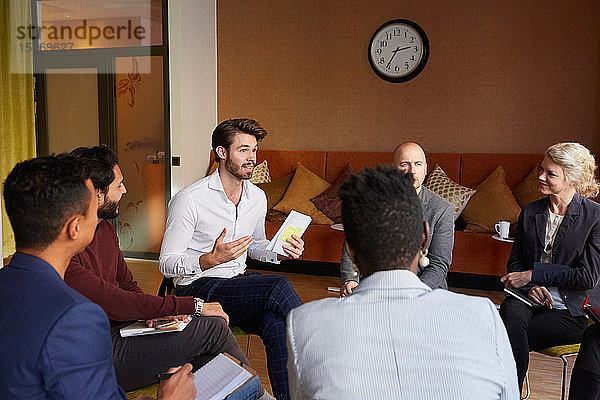 Männliche Unternehmer diskutieren im Kreis sitzend im Büro-Workshop mit Kollegen