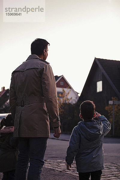 Rückansicht des Sohnes  der auf den Vater zeigt  während er bei Sonnenuntergang auf dem Fußweg neben ihm steht
