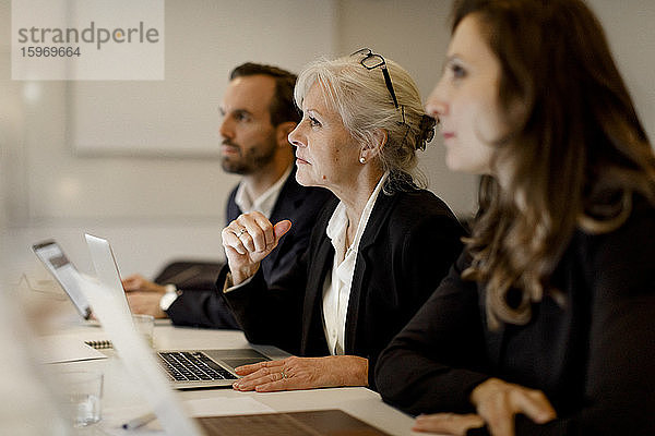 Reife Geschäftsfrau sitzt mit Kollegen am Konferenztisch in Bürobesprechung