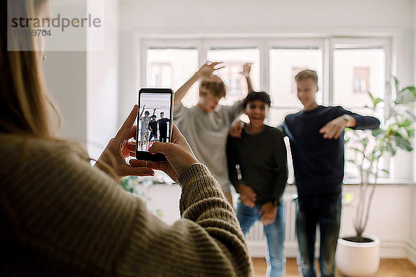 Teenagerin mit Handy filmt männliche Freunde beim Tanzen im Wohnzimmer