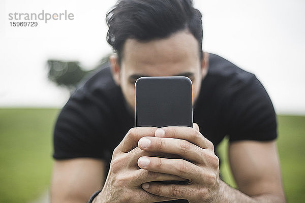 Junger Mann fotografiert durch Smartphone gegen den Himmel