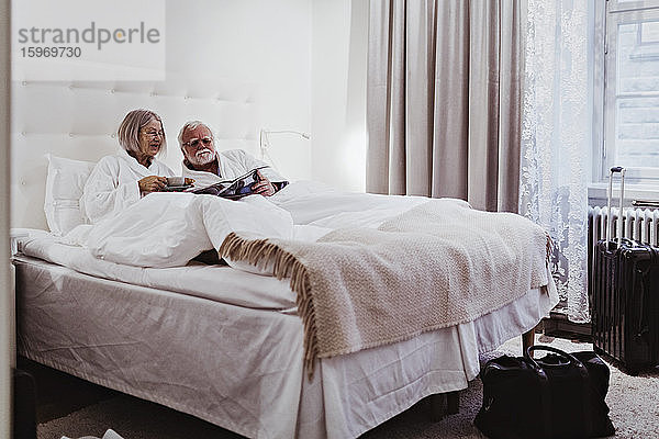 Ältere Frau liest Zeitung  während ein Mann Kaffee trinkt und sich im Hotel im Bett entspannt