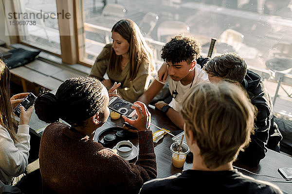 Hochwinkelaufnahme einer Teenagerin  die Kaffee fotografiert  während sie mit Freunden im Café sitzt