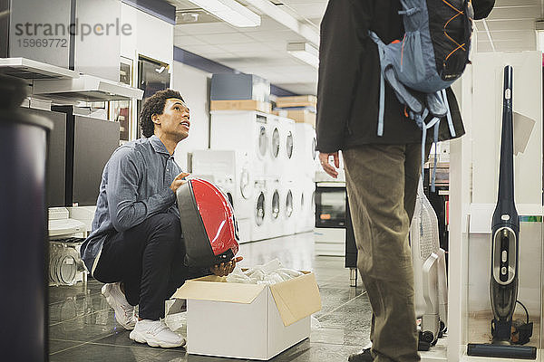 Junger Verkäufer zeigt einem männlichen Kunden im Laden ein Gerät