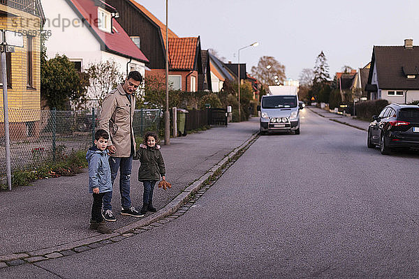 Vater steht im Herbst mit Kindern auf dem Bürgersteig