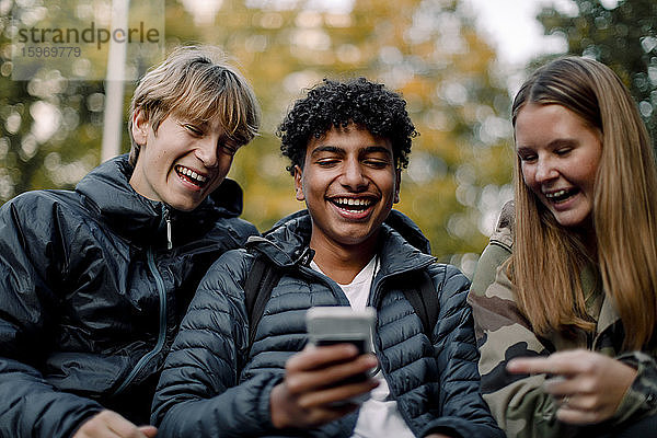 Glücklicher Teenager zeigt Freunden und Freundinnen in der Stadt ein Smartphone