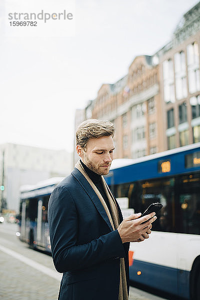 Selbstbewusster Unternehmer surft in der Stadt mit einem Smartphone im Netz