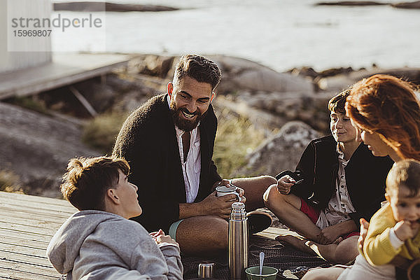 Lächelnder Vater mit Familie sitzt im Sommer vor der Hütte