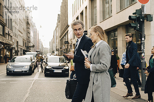 Seitenansicht eines weiblichen Geschäftsmannes mit einem männlichen Mitarbeiter beim Überqueren der Straße in der Stadt