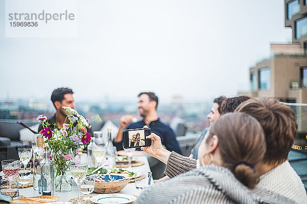 Lächelnde Freundinnen  die während der Party auf der Terrasse sitzen und sich am Telefon selbstständig machen