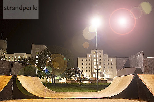 Junger Mann fährt nachts Skateboard auf Skatepark-Rampe