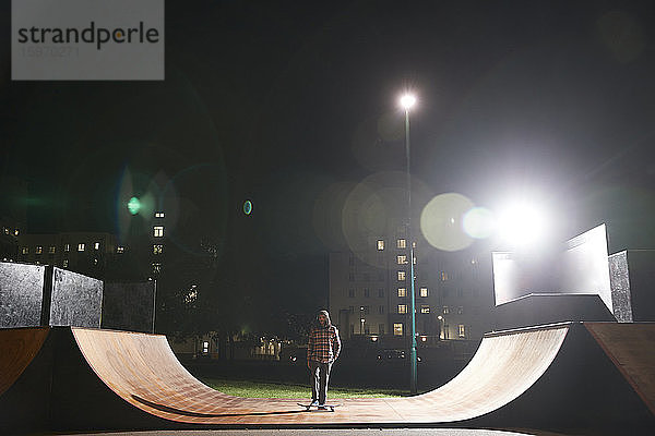 Junger Mann fährt nachts Skateboard auf der Rampe im Skatepark