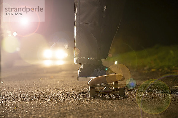 Junger Mann beim Skateboarden im Scheinwerferlicht am Straßenrand