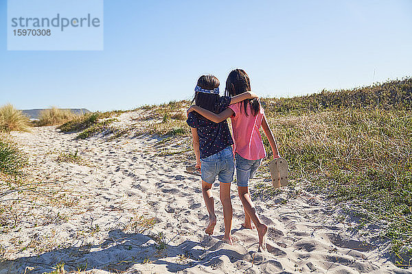 Glückliche  liebevolle Schwestern spazieren am sonnigen Strand