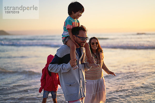 Glückliche Familie watet bei Sonnenuntergang im Meer