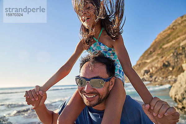 Glücklicher Vater trägt Tochter auf den Schultern am sonnigen Strand