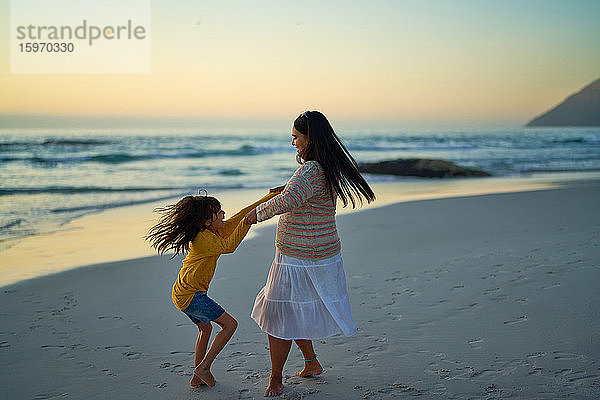 Glückliche Mutter und Tochter drehen sich bei Sonnenuntergang am Meeresstrand