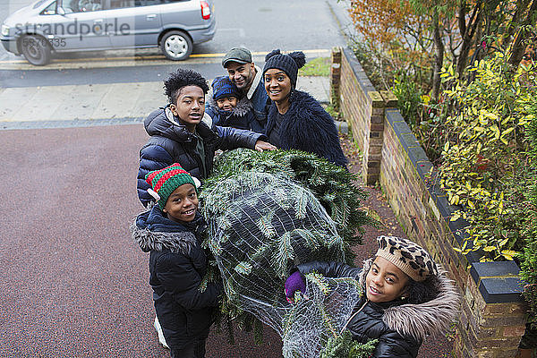 Familie trägt Weihnachtsbaum in Einfahrt